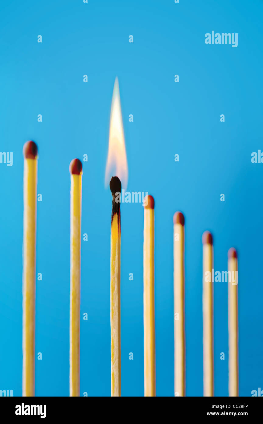 A burning match in a row of unlit matches Stock Photo
