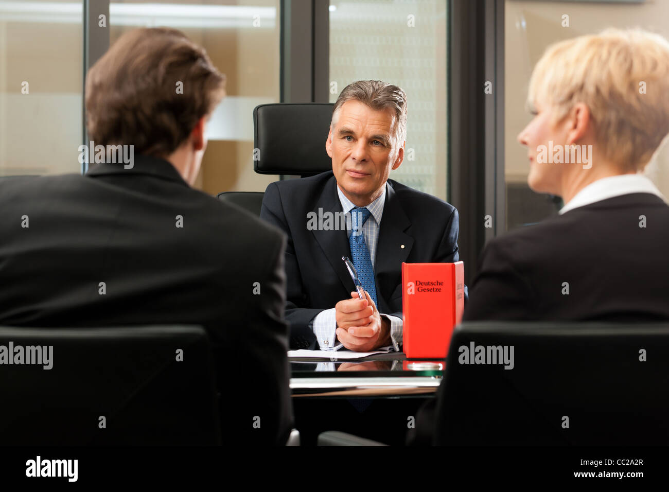 Mature lawyer or notary with clients in his office in a meeting Stock Photo