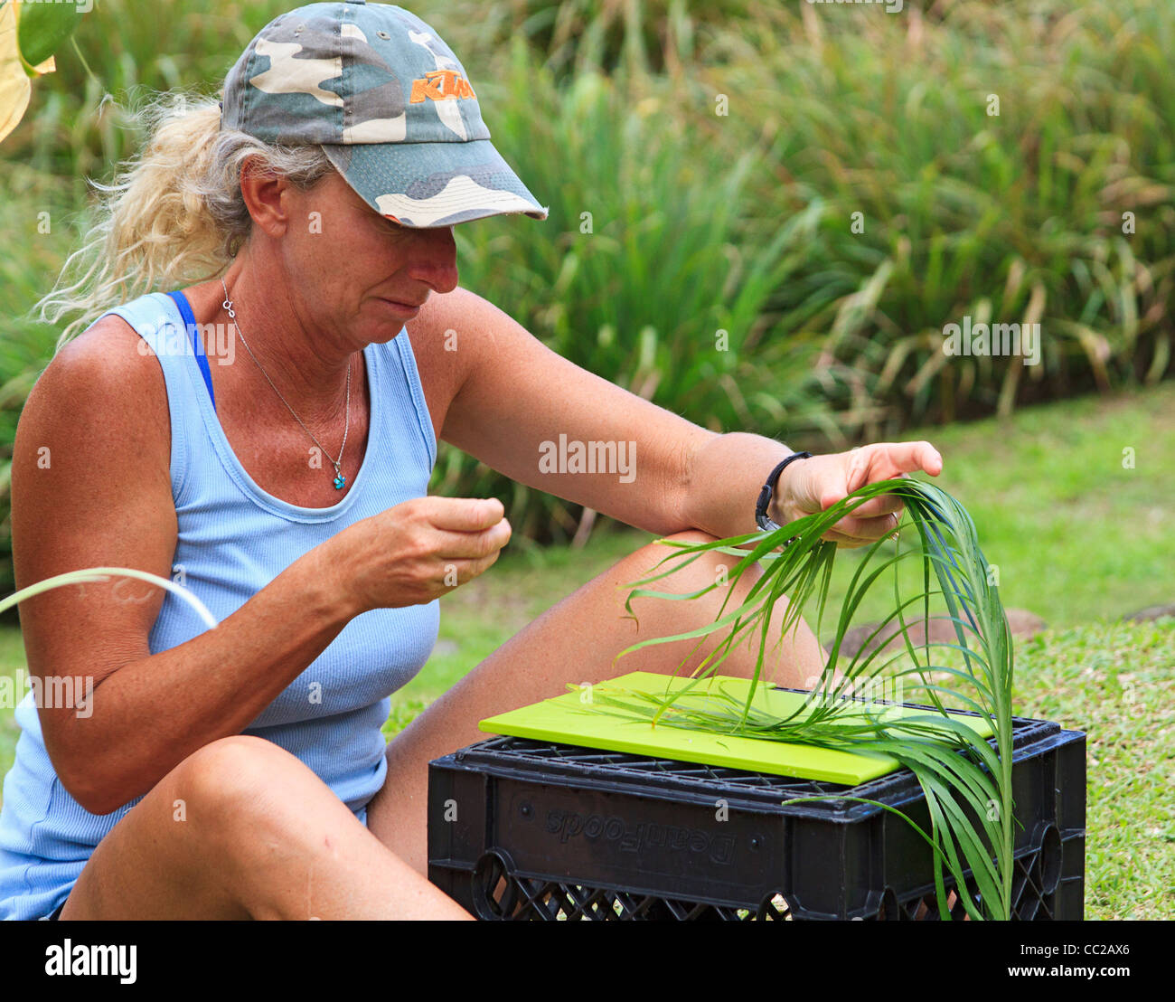 Woman visitor tries her hand at making a traditional lei, not from flowers but from ti leaves. Halawa Valley, Molokai, Hawaii Stock Photo