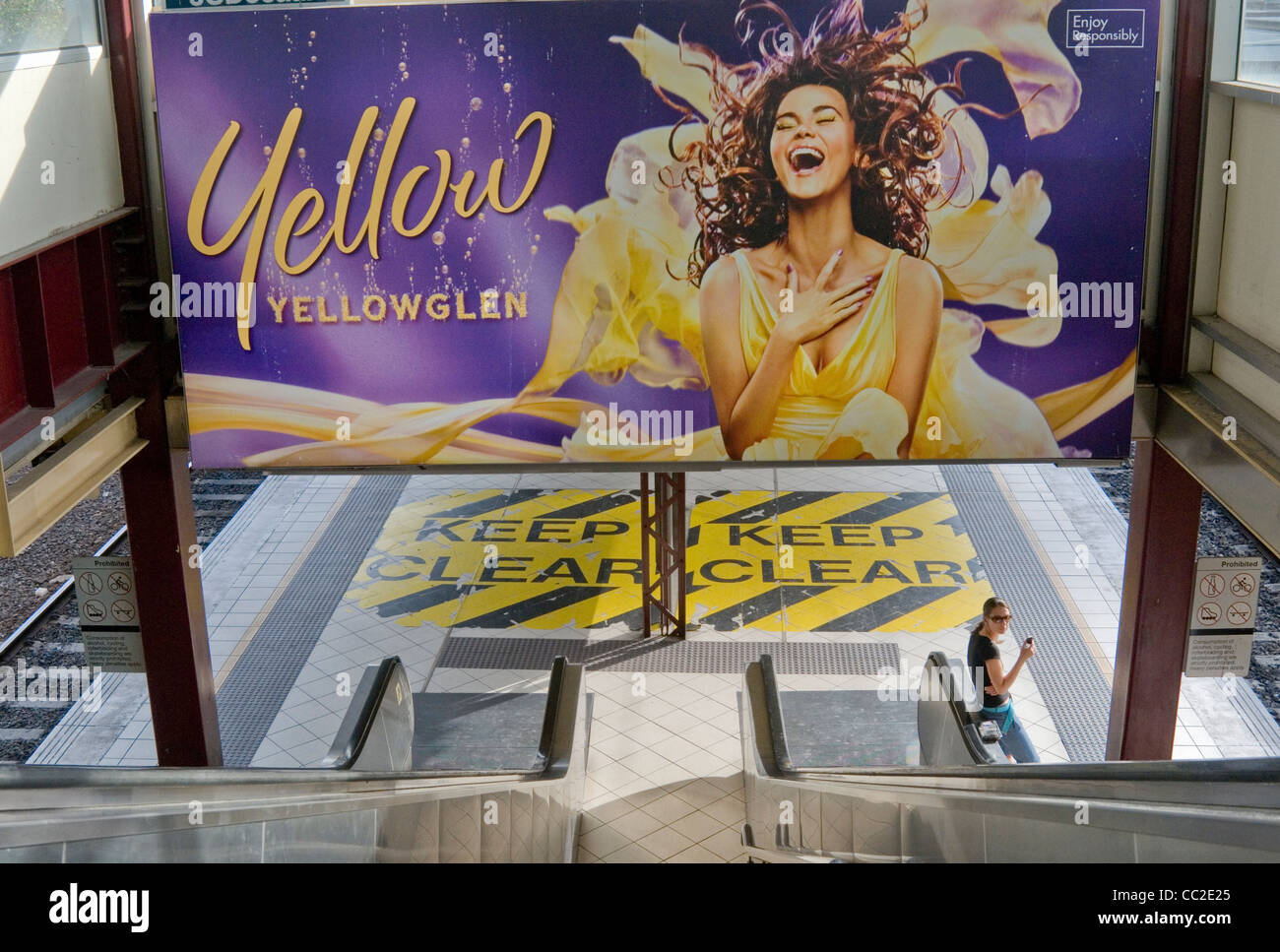Woman waiting on a station platform is dwarfed by a billboard advertising sparkling wines, Melbourne, Australia Stock Photo