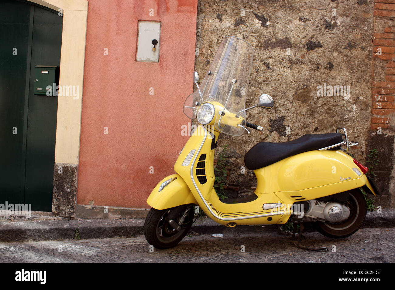 A yellow scooter parked outside of a small Italian door in Sicily, Italy. Stock Photo