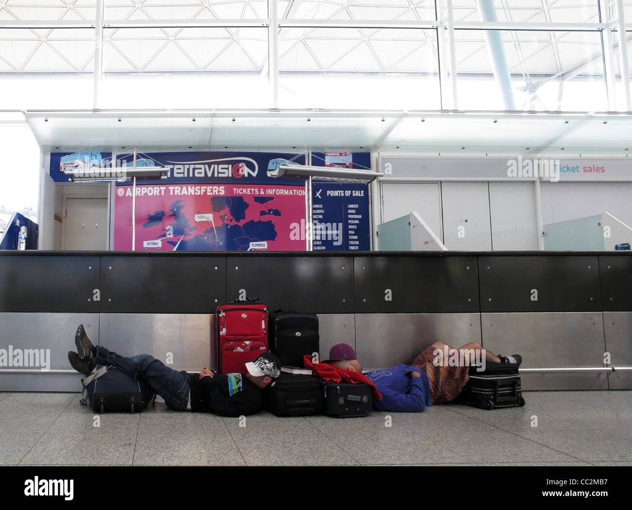 Exhausted travelers wait sleepily for an airport transfer desk to open, at London Stansted Airport Stock Photo