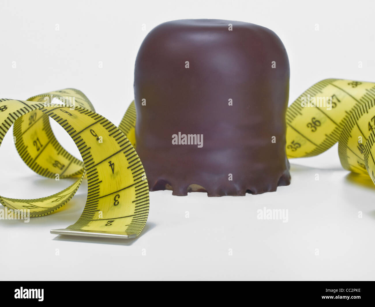 Detail photo of a small chocolate-covered cream cake, beside is a measuring tape Stock Photo