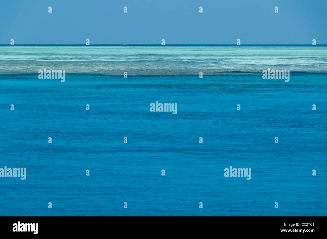 A view of the horizon on the Great Barrier Reef, Australia. The blue water in the bottom part of the frame is deeper water with a mostly sandy bottom. Beyond that, the darker area is a mix of shallow reef and sand just below the surface of the water. The shallow reef provides a natural barrier against waves and swells. This particular shot was taken about 150 miles northeast of Gladstone on Swains Reef, about 115 miles offshore. Stock Photo