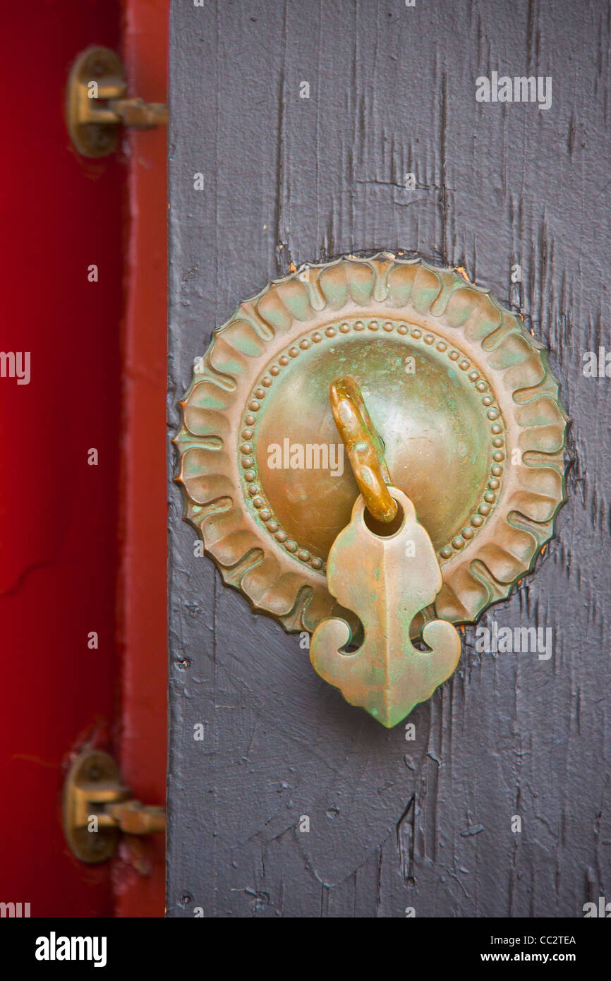 ancient solar Chinese bronze knob with an arrow handle and 2 hinges on a wood door painted in gray and red Stock Photo