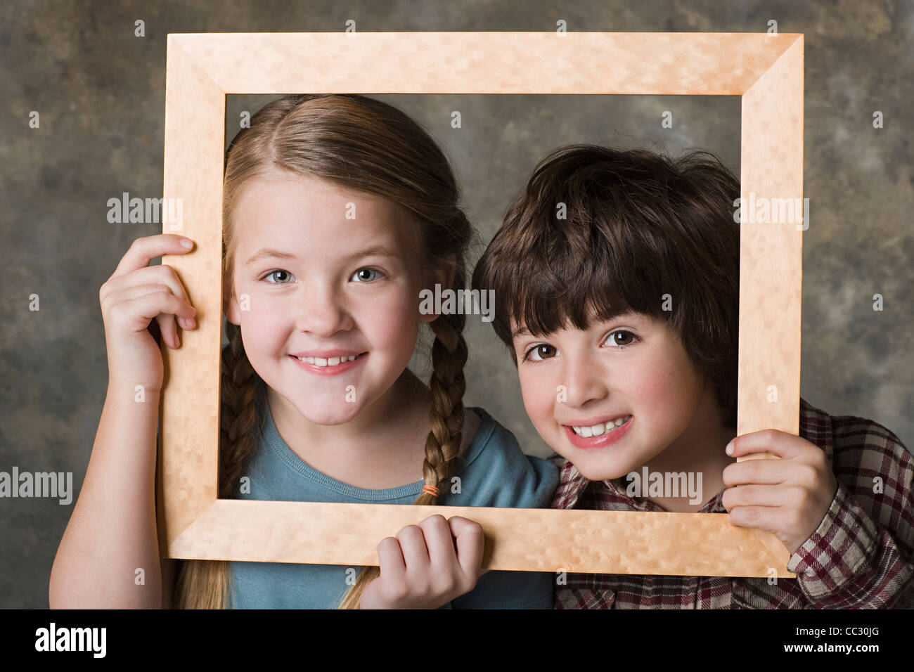 Portrait of girl (8-9) and boy (6-7) looking through frame, studio shot Stock Photo