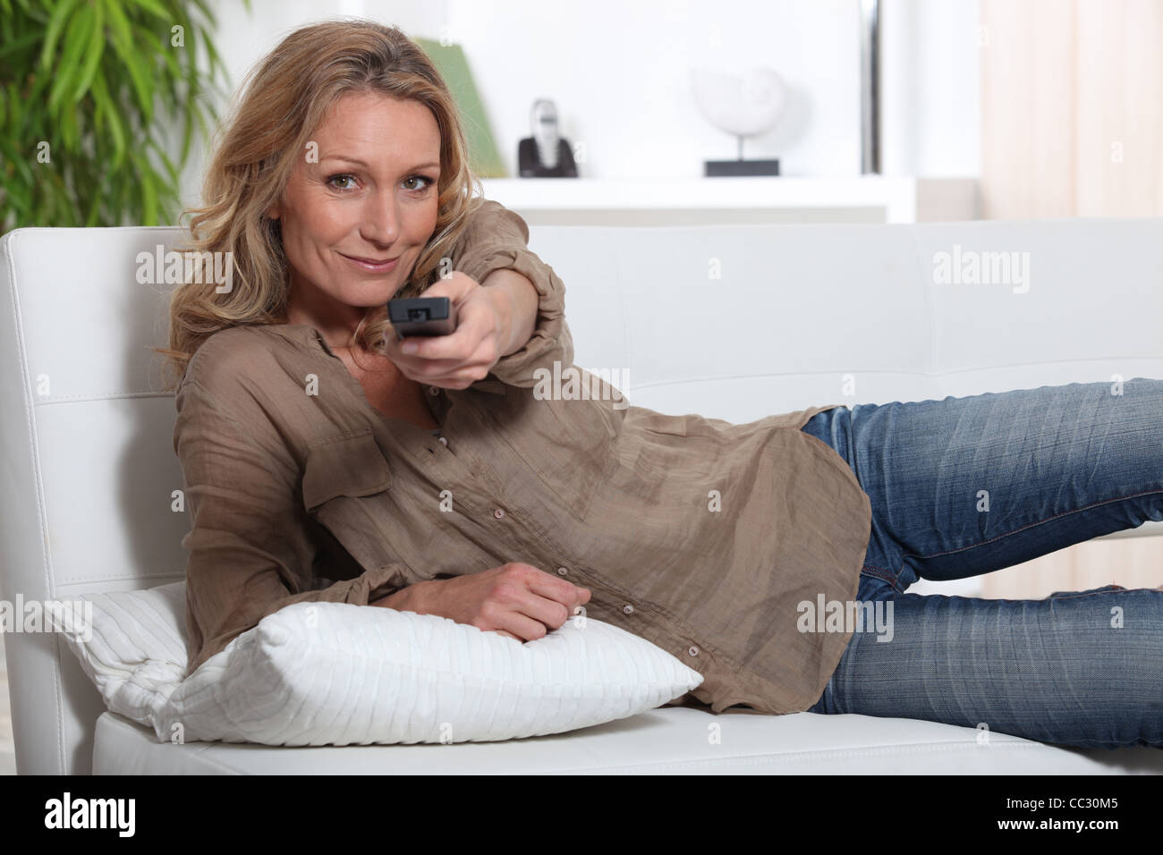 Woman laid on couch holding television remote control Stock Photo - Alamy