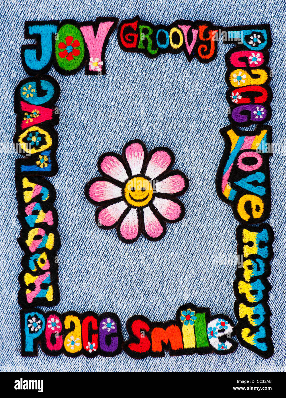 Embroidery iron on patches of Multicoloured Love, Peace, Happy words with a smiley face flower on a denim jean background Stock Photo