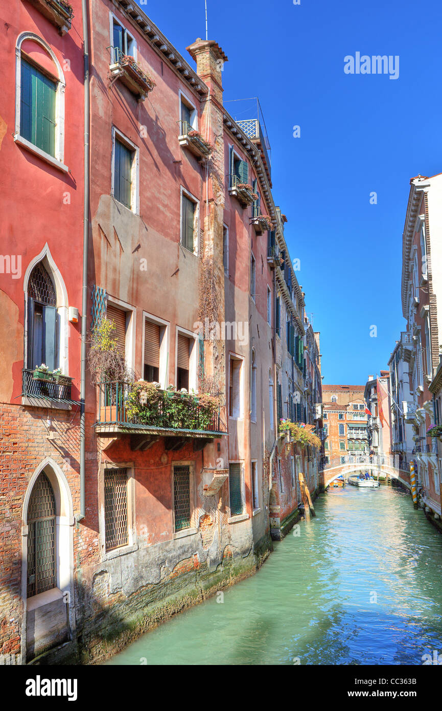 Vertical oriented image of small narrow canal among ancient houses under blue sky in Venice, Italy. Stock Photo