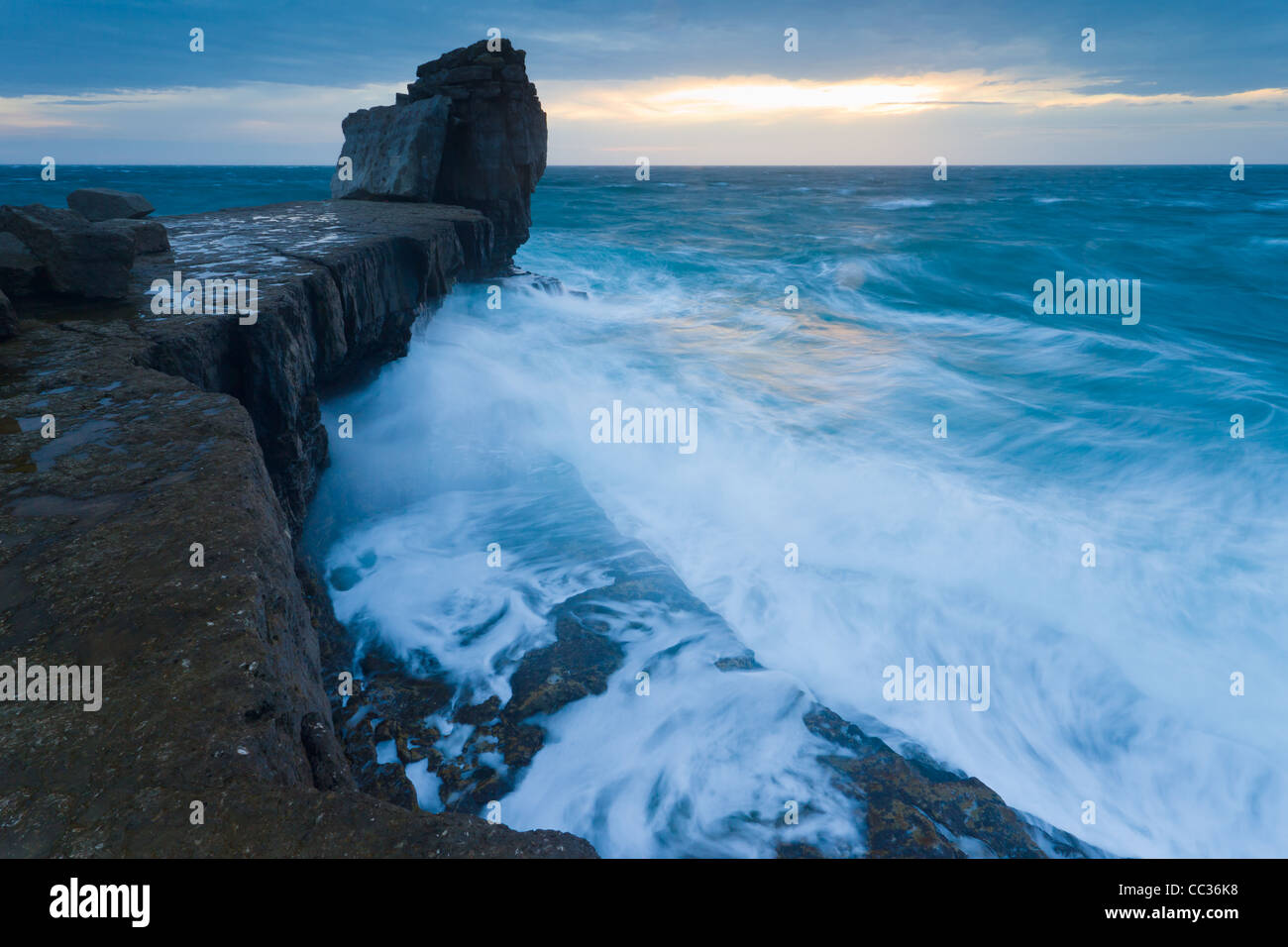 Waves crash over Pulpit Rock, at the tip of Portland Bill, Dorset, as the sun sets in November. Stock Photo