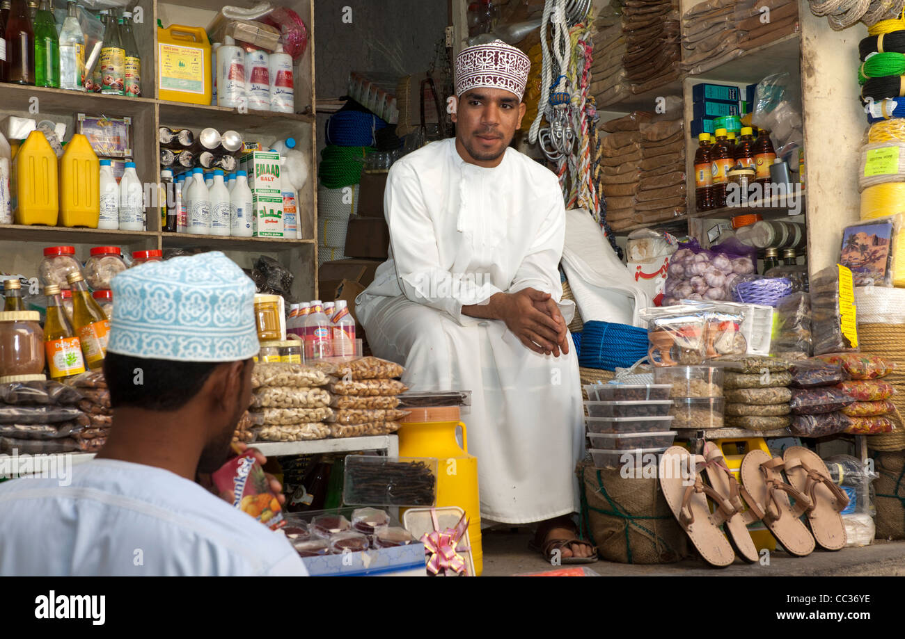 An Arab merchant sitting among his merchandise at a market stall on the bazar of Nizwa, Sultanate of Oman Stock Photo