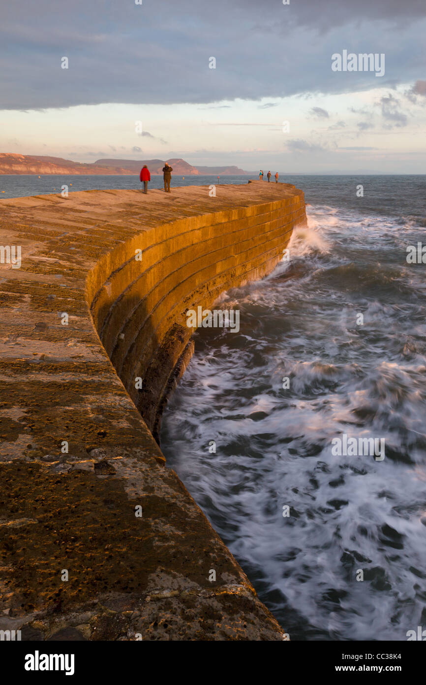 Walkers take in the fresh sea air and the view from the Cobb at sunset, Lyme Regis, November 2011 Stock Photo