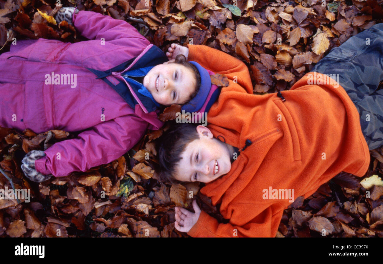 Boy and Girl lying in autumn leaves on ground Stock Photo - Alamy