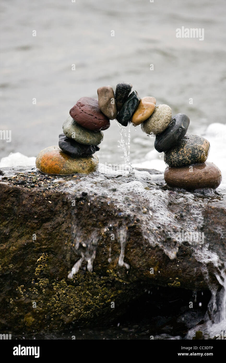 Balanced stones in a rock arch dripping water at the seaside after being struck by a wave at high tide. Stock Photo