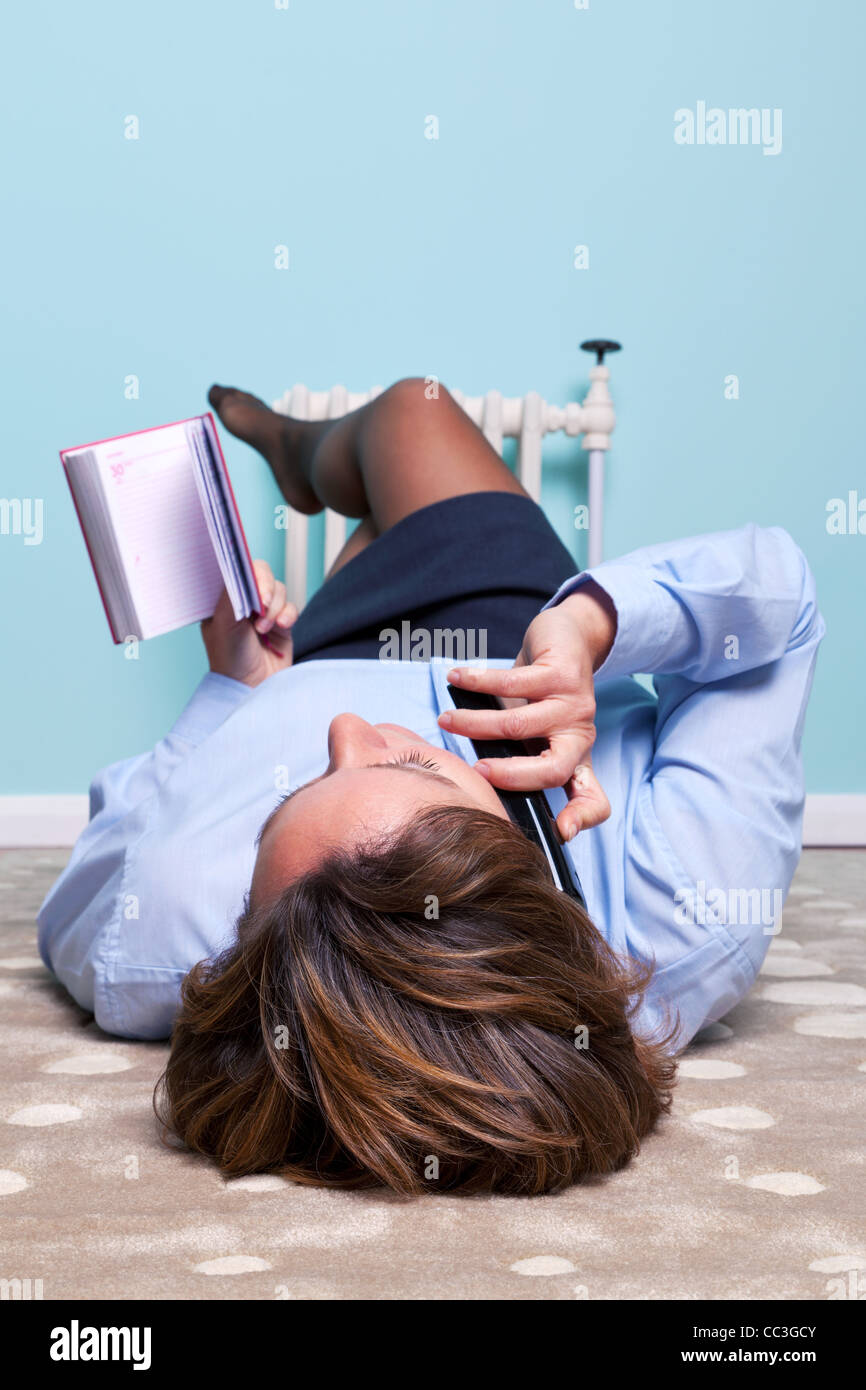 Photo of a businesswoman relaxed at home lying on a rug making a phone call with her diary in her hand, focus is on her head. Stock Photo
