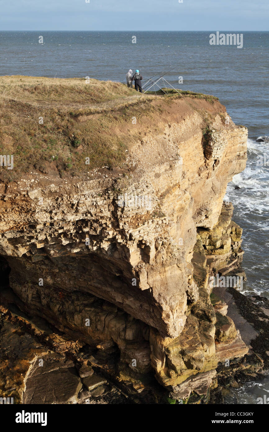 Two men line fishing off dangerous cliffs on the north sea coast near to South Shields, north east England UK Stock Photo