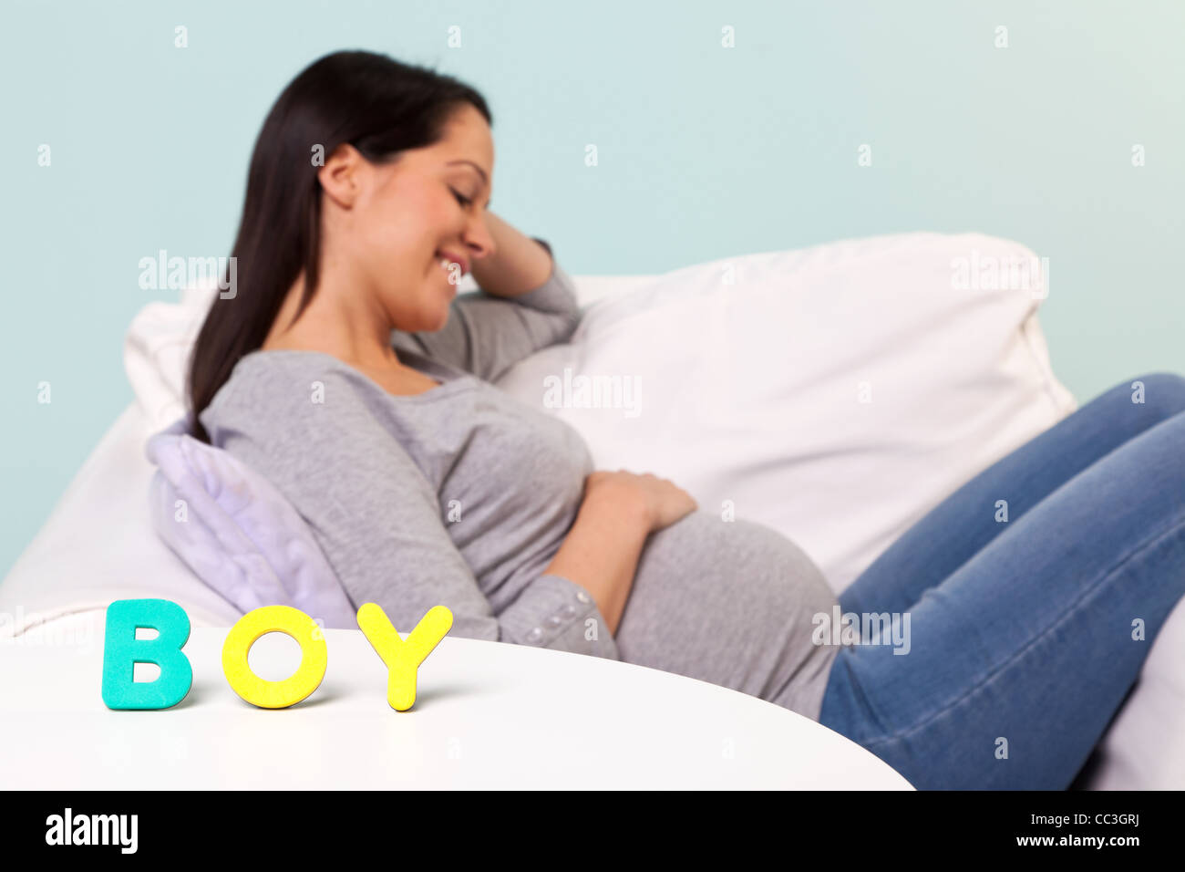 Photo of a pregnant woman at home sitting in an armchair, focus on the word BOY on the table in front. Stock Photo