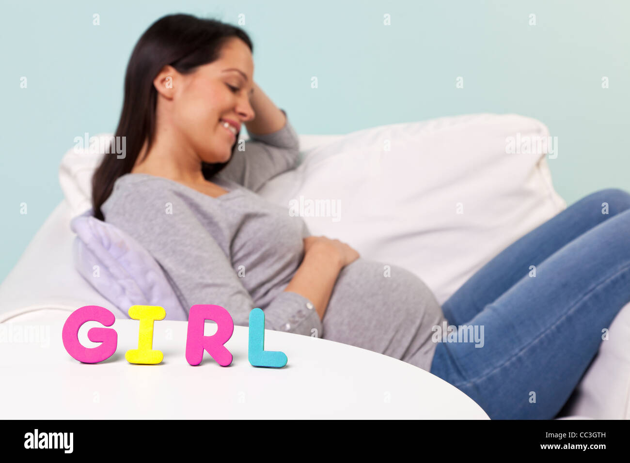 Photo of a pregnant woman at home sitting in an armchair, focus on the word GIRL on the table in front. Stock Photo