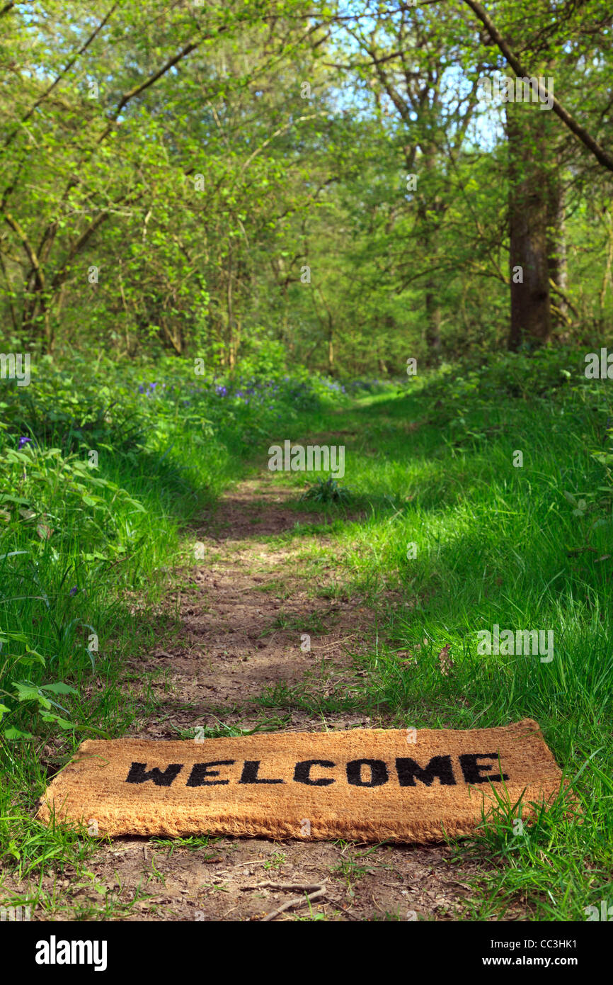 Concept photo of a Welcome doormat on a woodland footpath during springtime in vertical format. Stock Photo