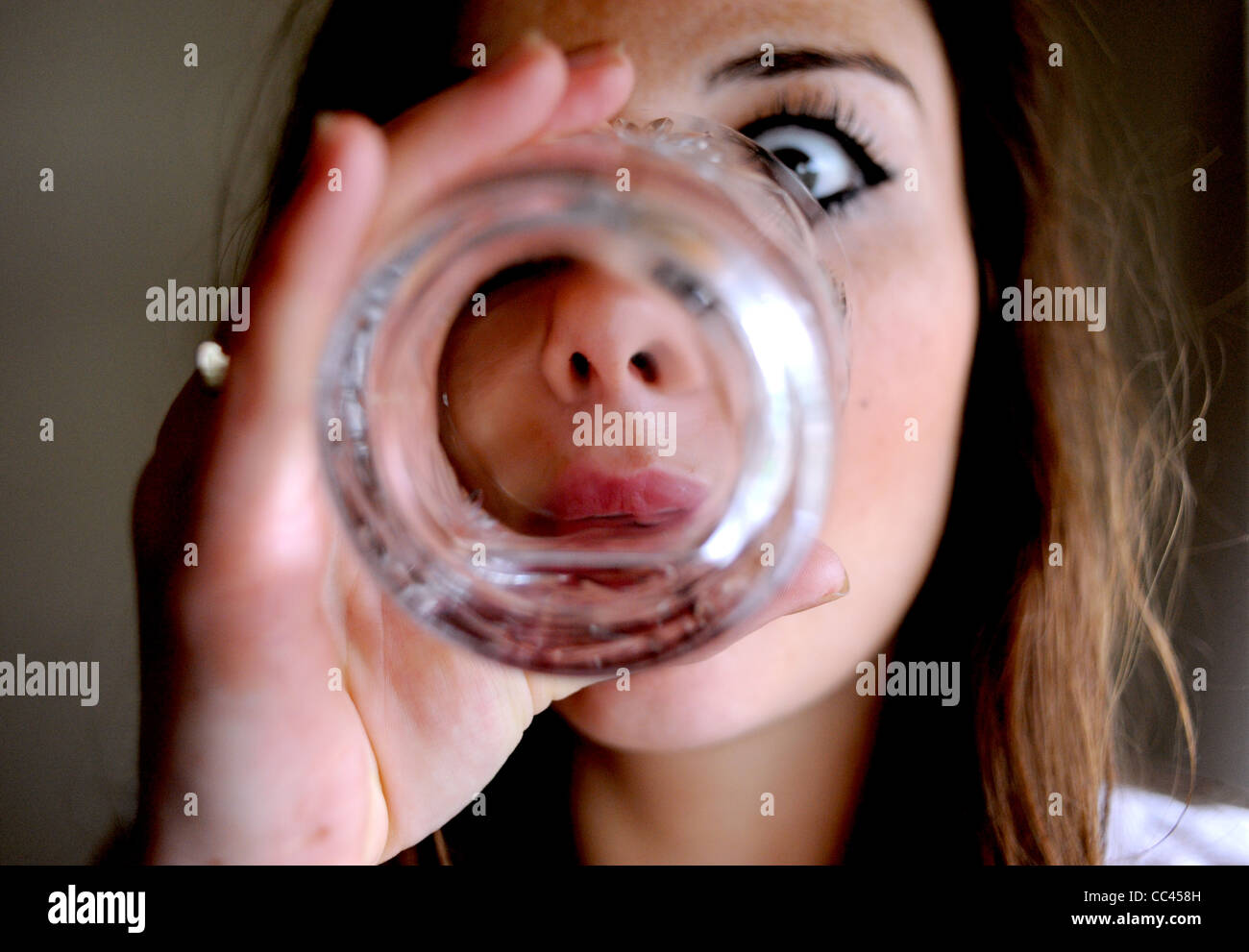 looking at life through the bottom of a glass - posed by model to illustrate alcohol abuse and young woman alcoholic Stock Photo