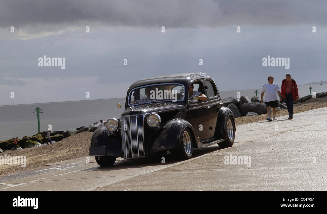 A lovely classic car, a Ford Pilot, cruises along the seafront at Folkestone during the 2011 NASC cruise. Angry skies after rain Stock Photo