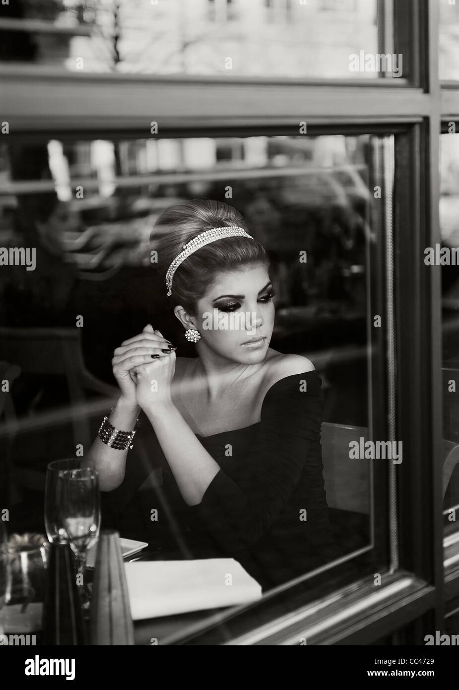 A woman waits patiently at a restaurant as she looks out the window, in black and white. Stock Photo
