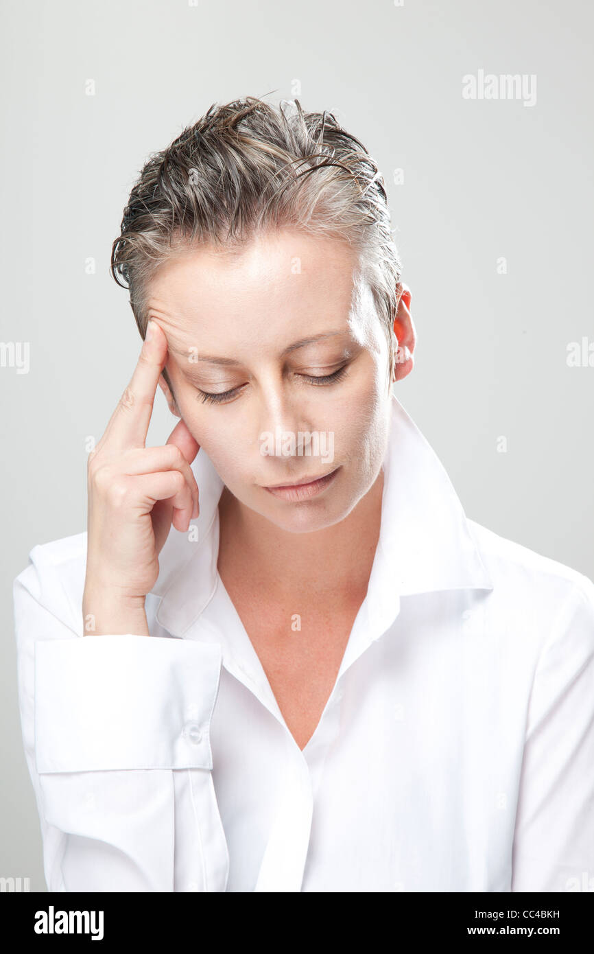 middle aged woman in white blouse holds her head while she thinks or concentrates or has a headache. Stock Photo