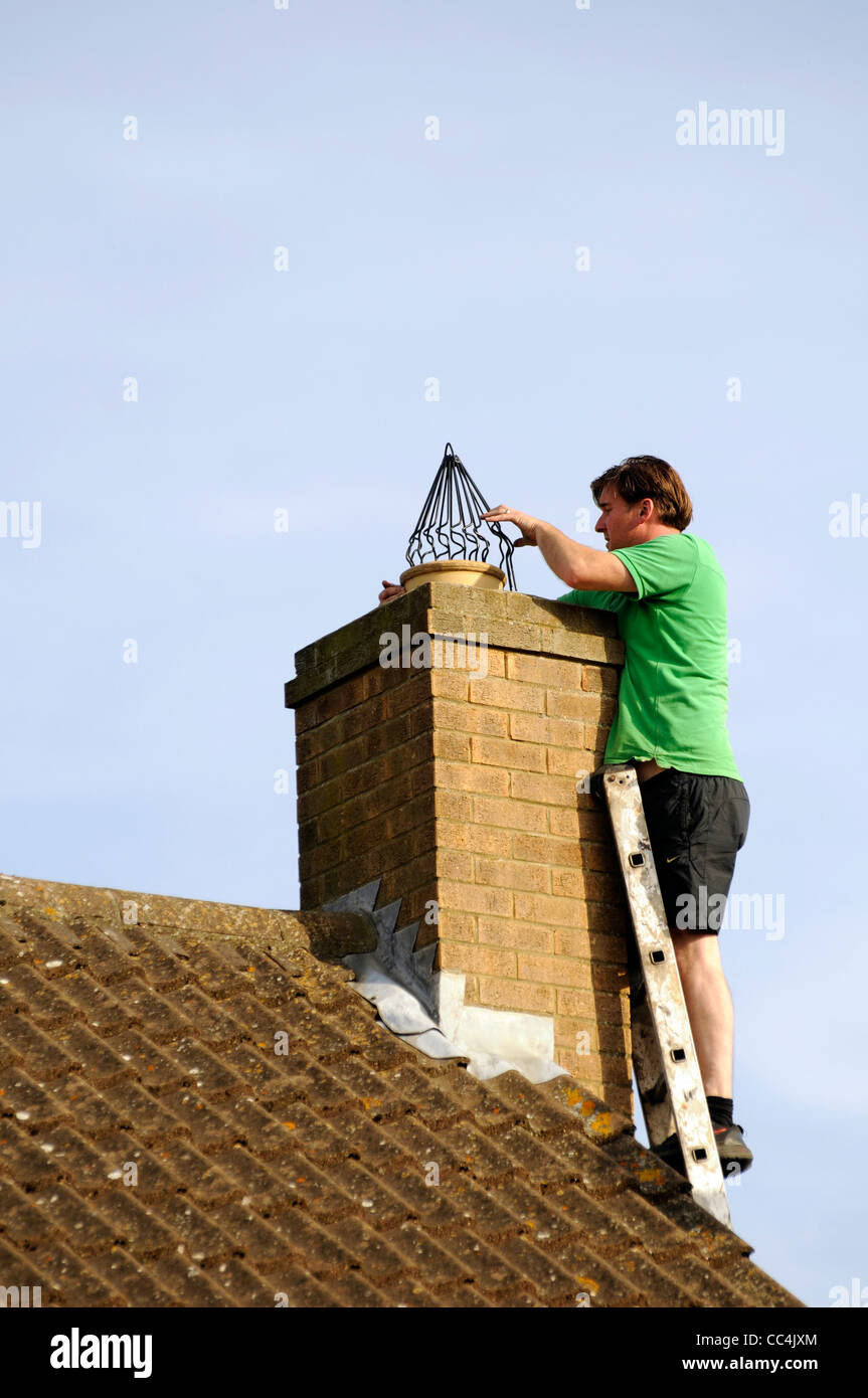 Man fitting chimney cowl (bird guard) to suburban house in UK Stock