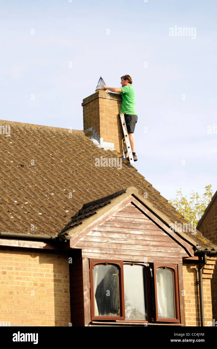 Man fitting chimney cowl (bird guard) to suburban house in UK. Stock Photo