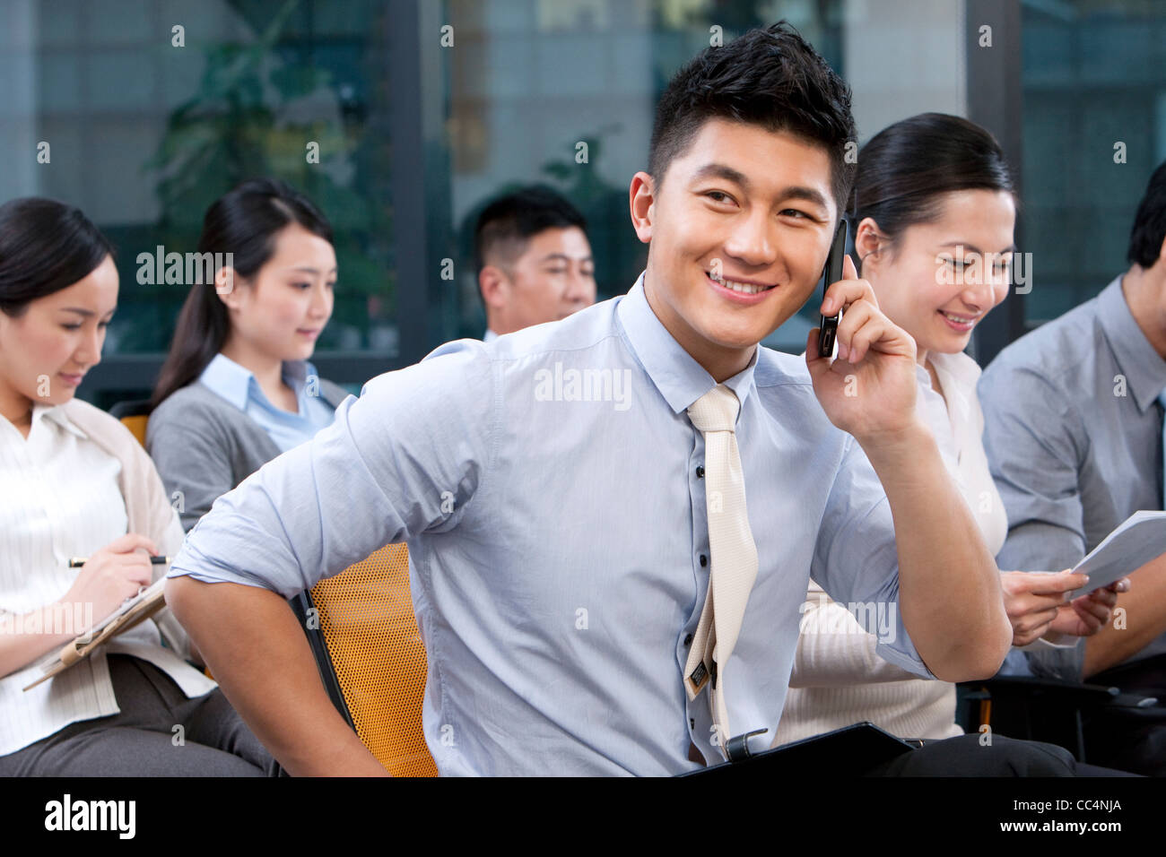 Businessman on his mobile phone with colleagues sitting in the background Stock Photo