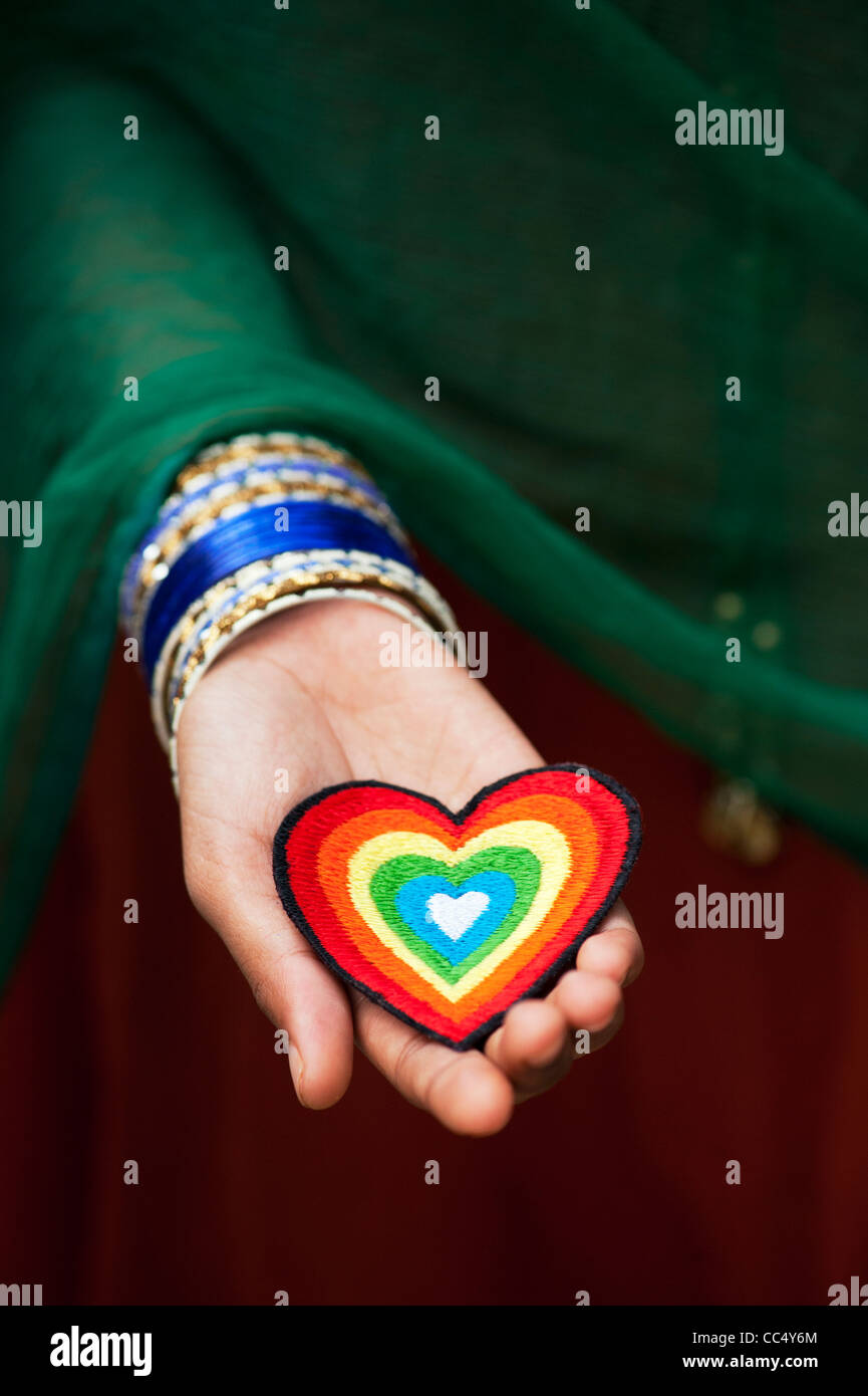 Indian girls hands holding an embroidery iron on patch of a multicoloured love heart. India Stock Photo