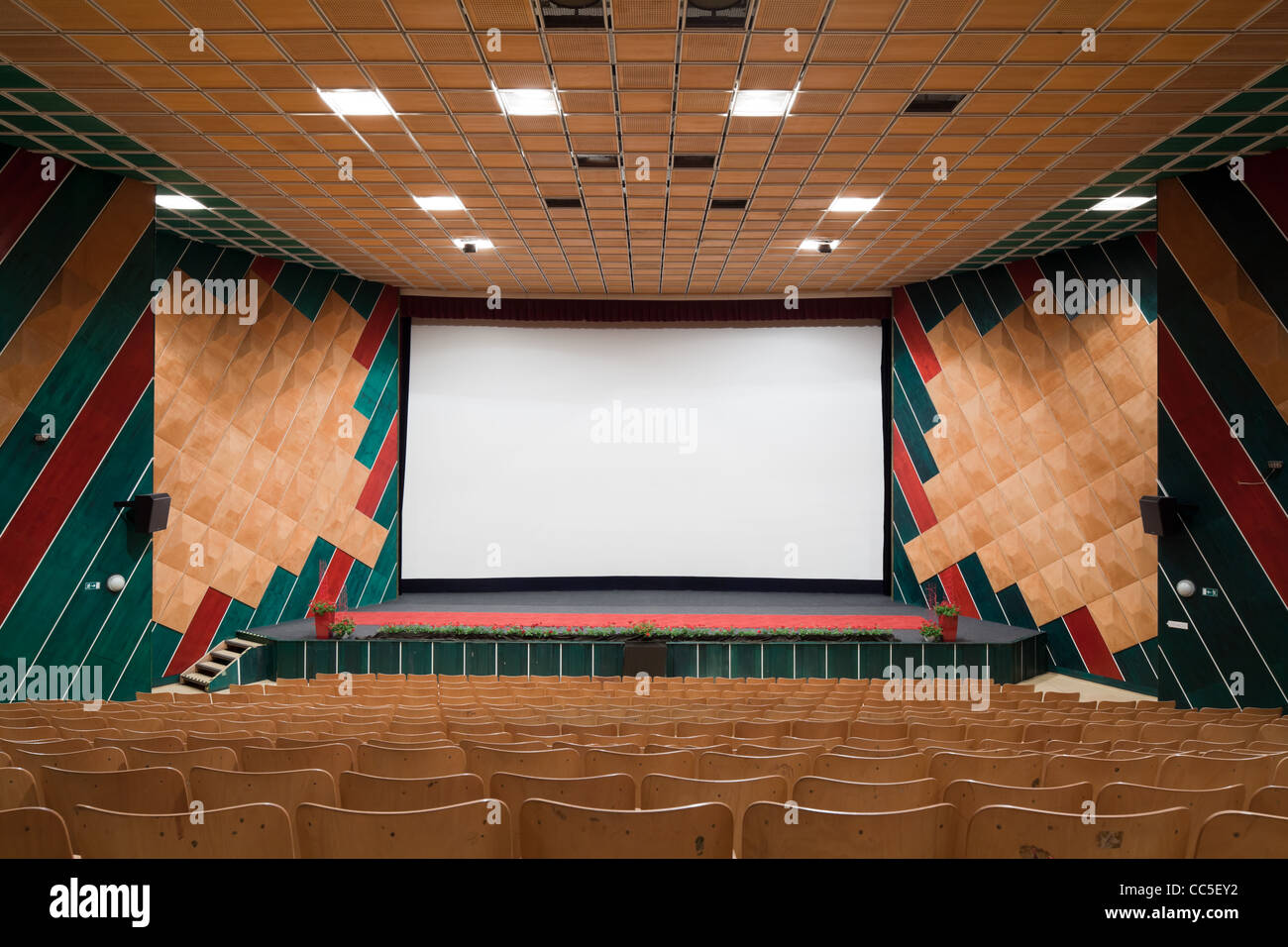 Empty cinema auditorium with line of chairs and projection screen. Ready for adding your own picture. Front view. Stock Photo