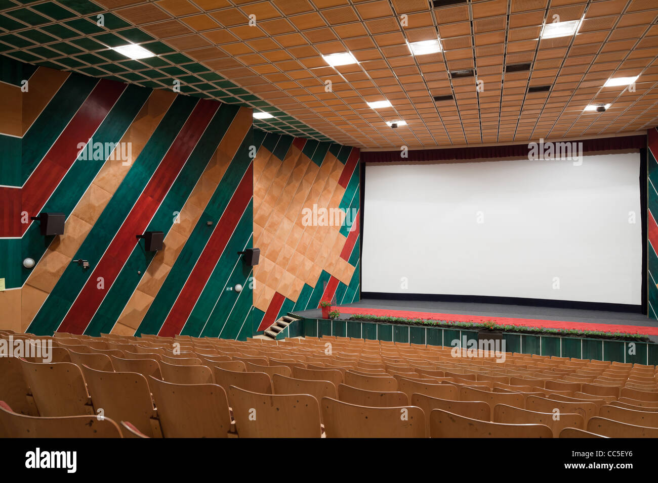 Empty cinema auditorium with line of chairs and projection screen. Ready for adding your own picture. Side view. Stock Photo