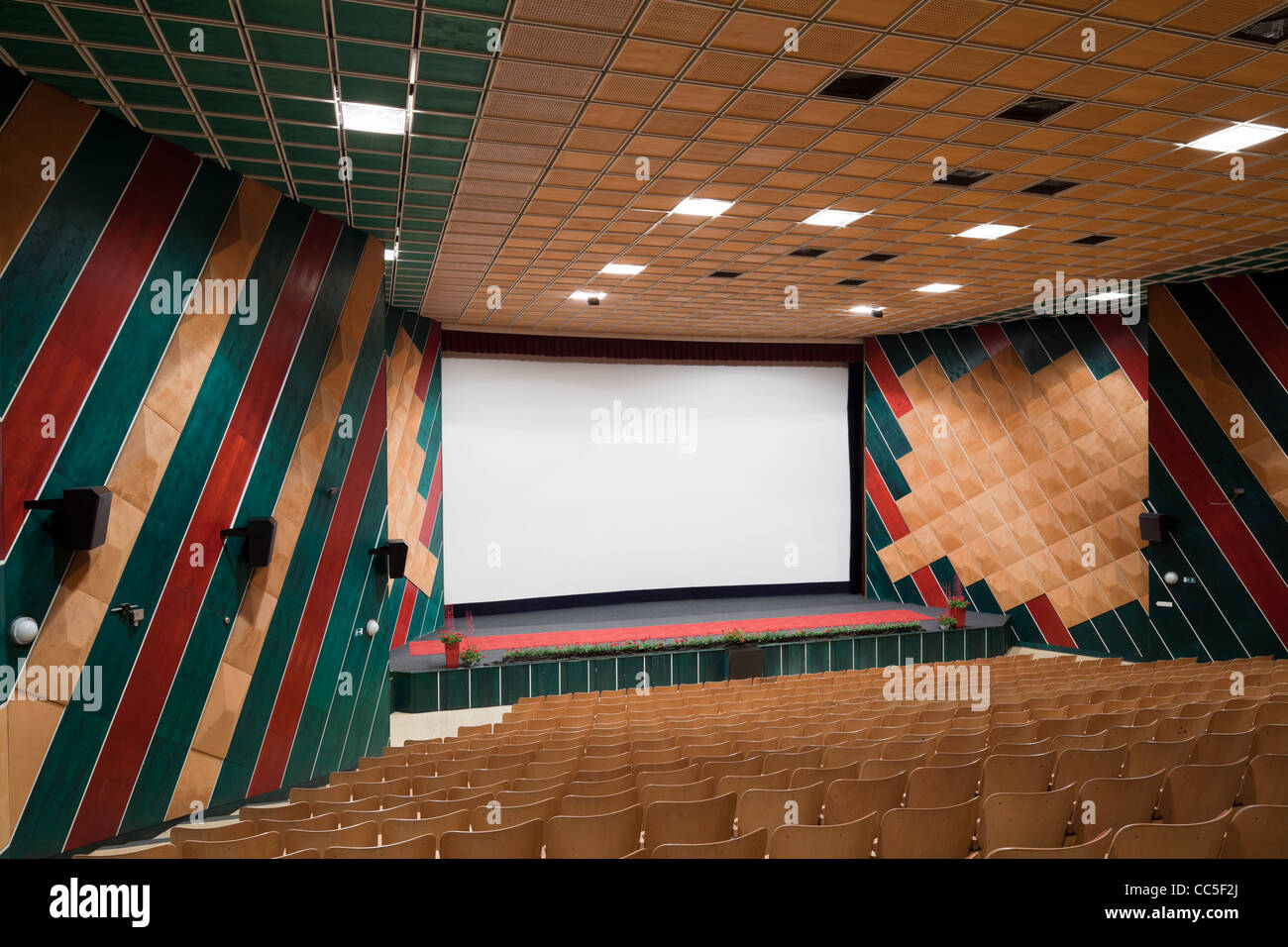Empty cinema auditorium with line of chairs and projection screen. Ready for adding your own picture. Side view. Stock Photo