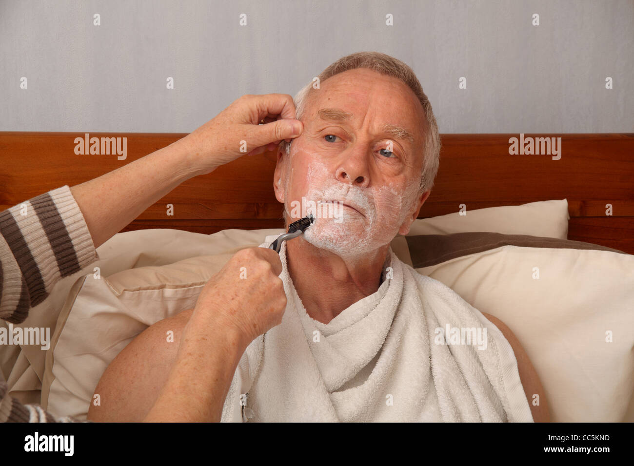 A bedbound man in his 60's being shaved by his wife/carer Stock Photo