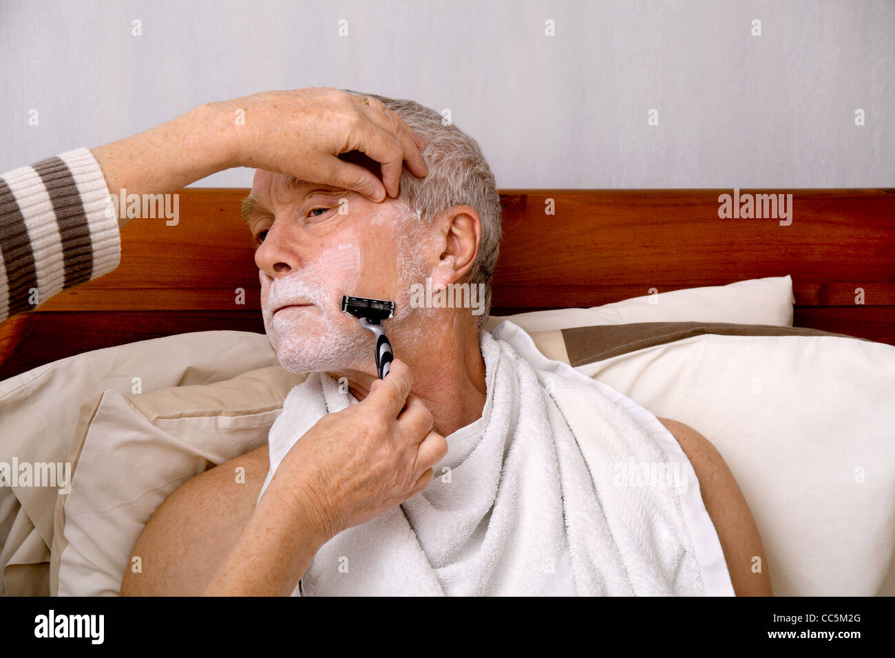 A man in his 60's being shaved by his wife/carer, at home in bed Stock Photo