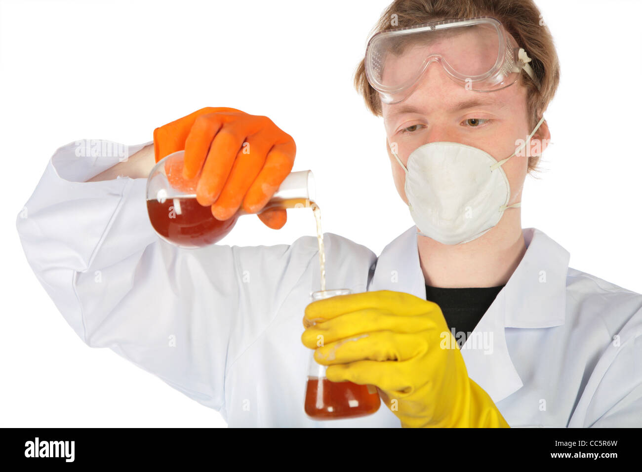 Scientist in respirator and rubber gloves pours brown liquid from one flask in another Stock Photo