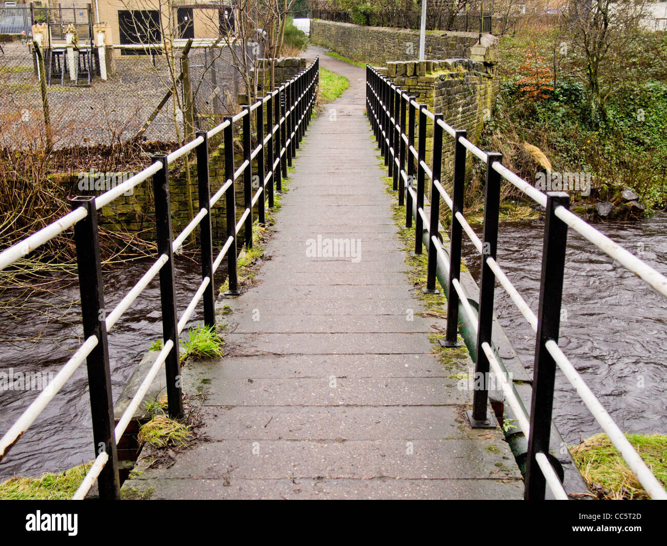 An iron and concrete bridge spanning a stream in Slaithwiate, West Yorkshire.  Alongside runs a green gas pipe Stock Photo