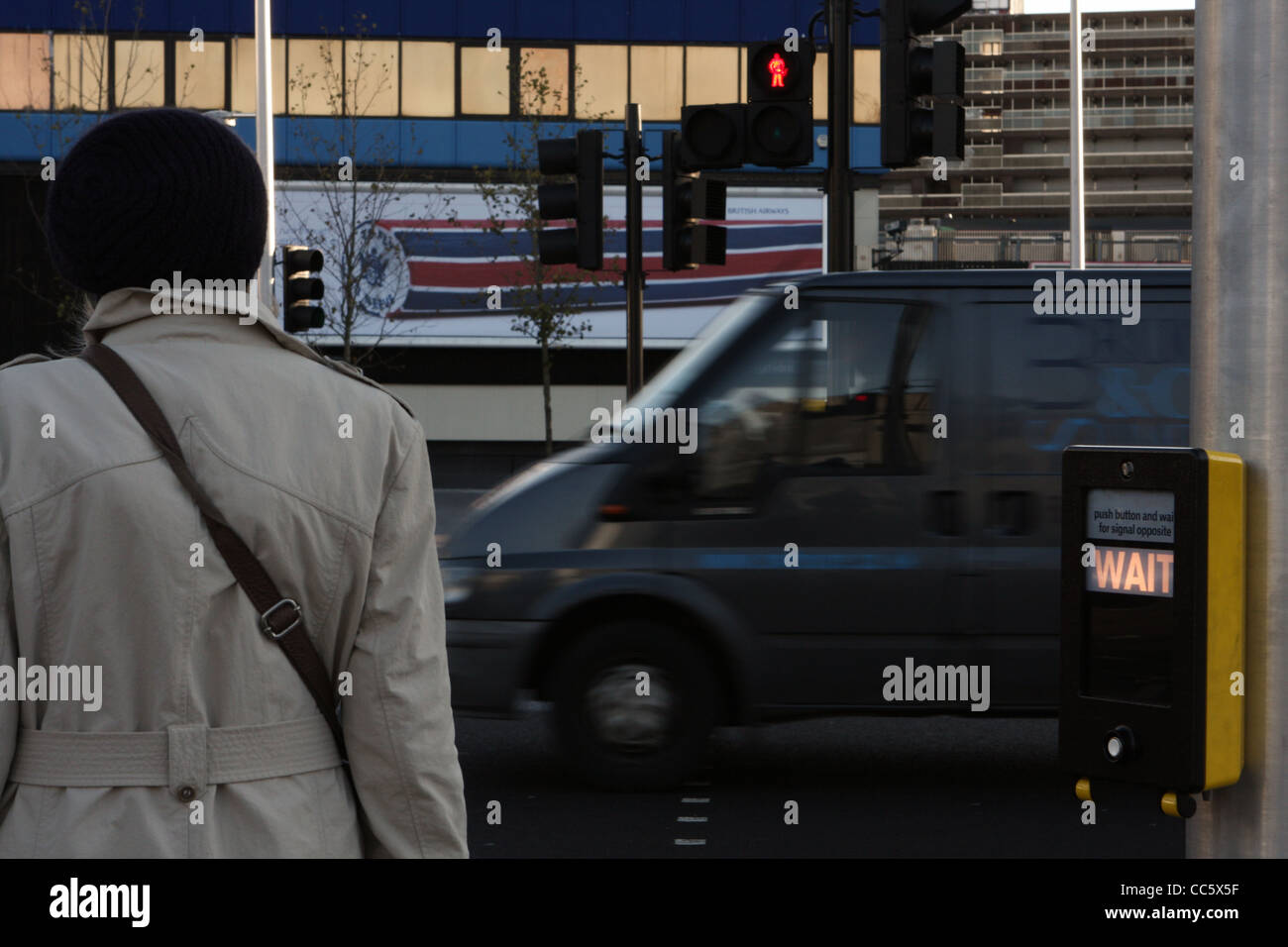 a woman waiting to cross the road at a pedestrian crossing in London ...