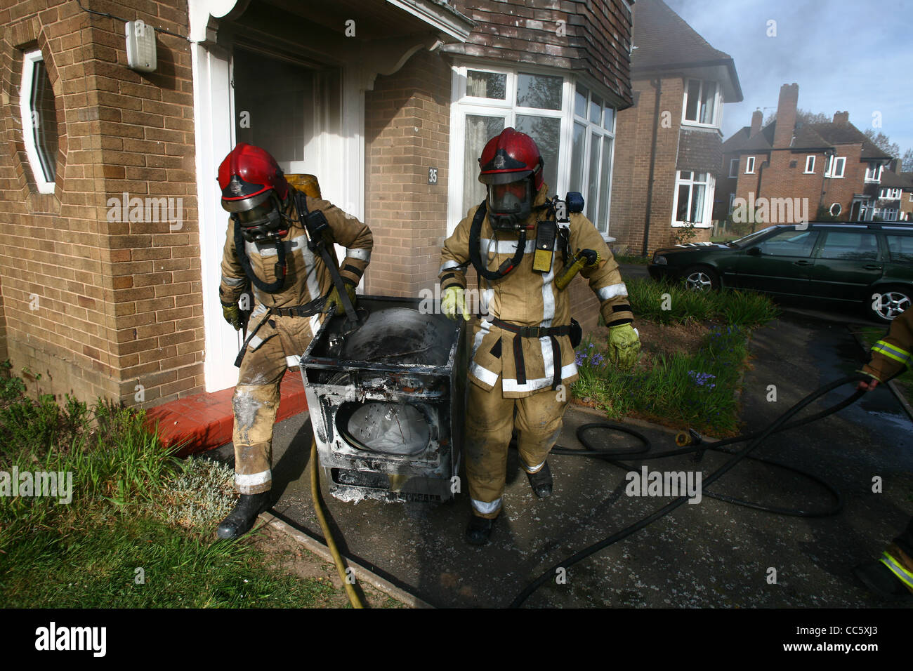 Two firefighters remove a fire damaged tumble dryer involved in a house fire. Stock Photo