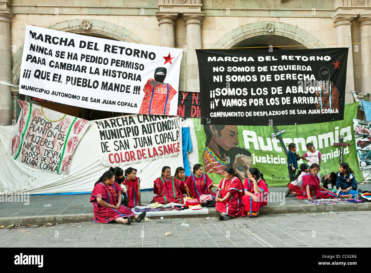 groups of Mexican Triqui Indian women & children against backdrop of banners strung between arches of Governors Palace Oaxaca Stock Photo