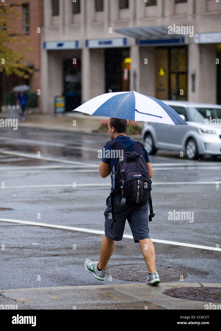 A young man crossing the street holding an umbrella on a rainy day Stock Photo