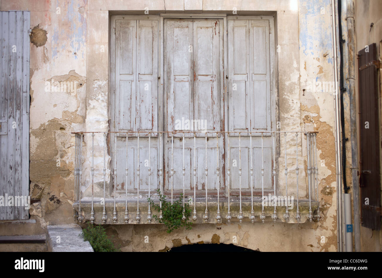 Three old wooden doors open up to a metal balcony railing in Menerbes, France Stock Photo