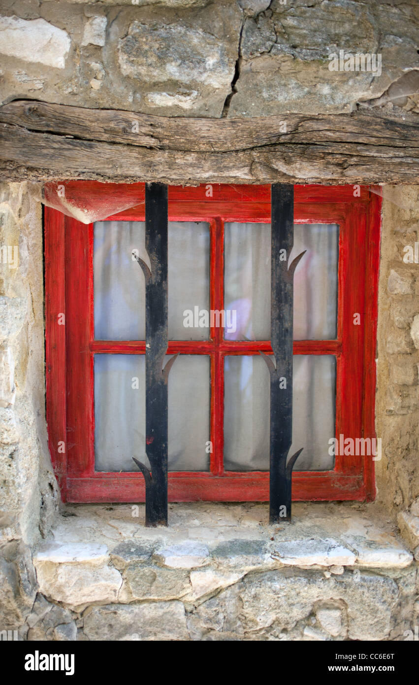 A small barred window with red wooden frame in Saignon, France Stock Photo