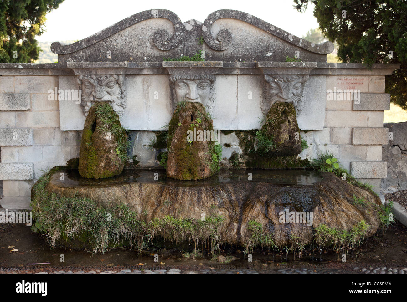 This interesting fountain / sculpture has three faces with moss coming out of their mouths - in Lourmarin, France Stock Photo