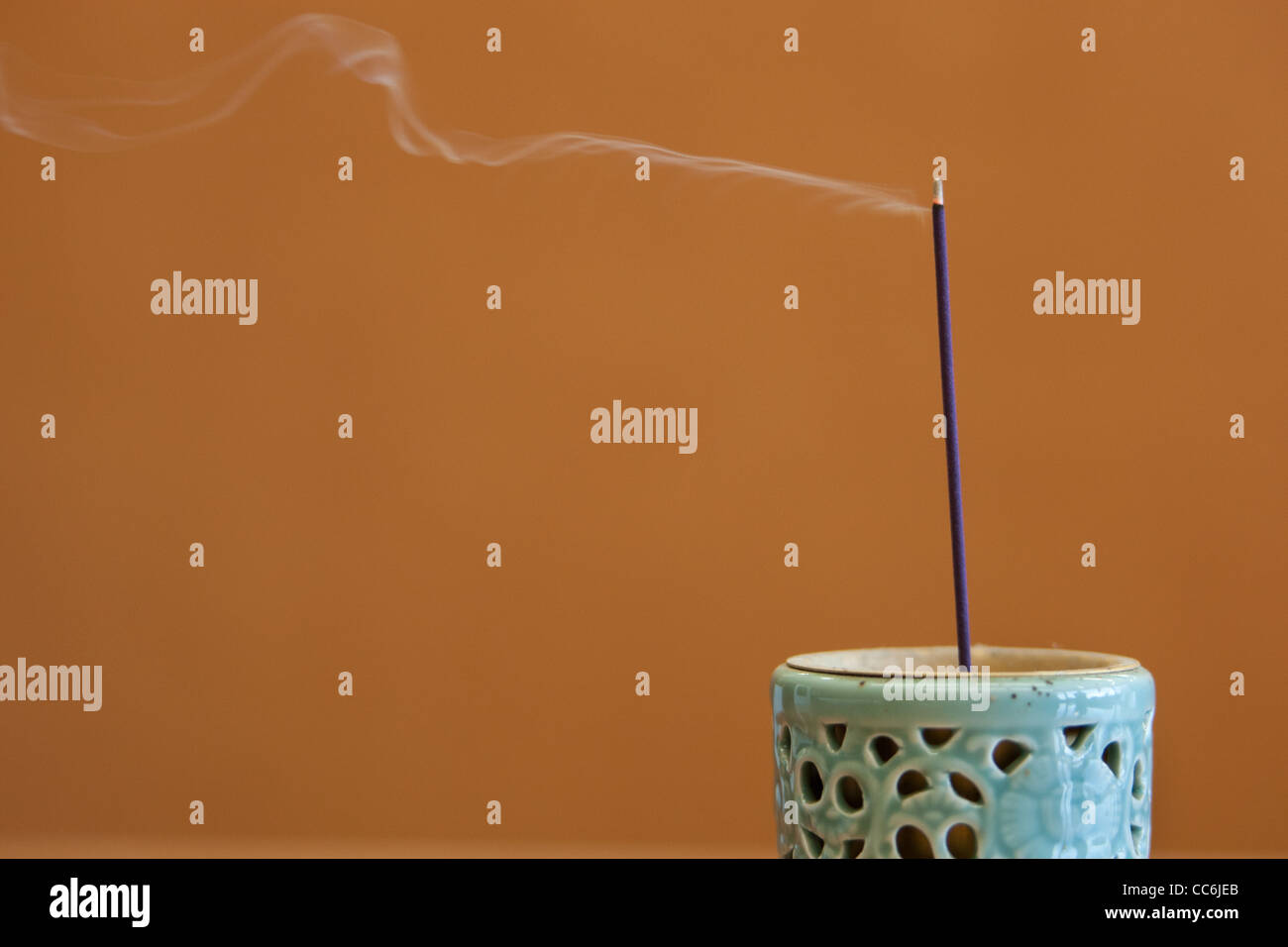 A stick of incense smolders and smokes in an incense burner pot. Stock Photo