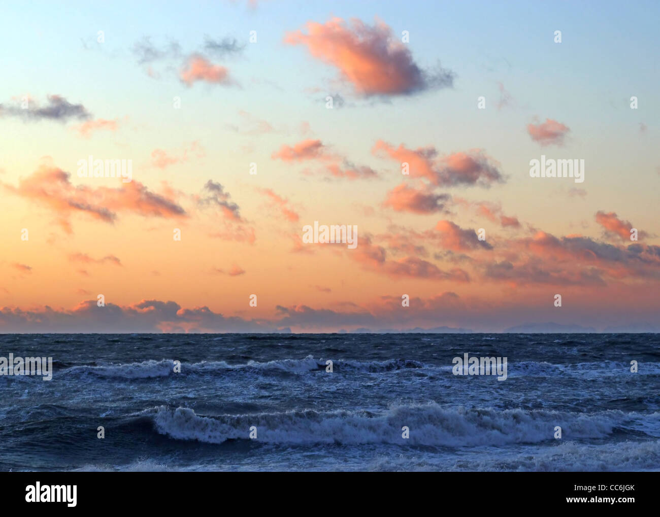 Interesting orange clouds at sunset over the ocean waves. Stock Photo