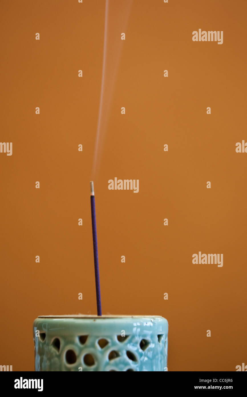 A stick of incense smolders and smokes in an incense burner pot Stock Photo Alamy