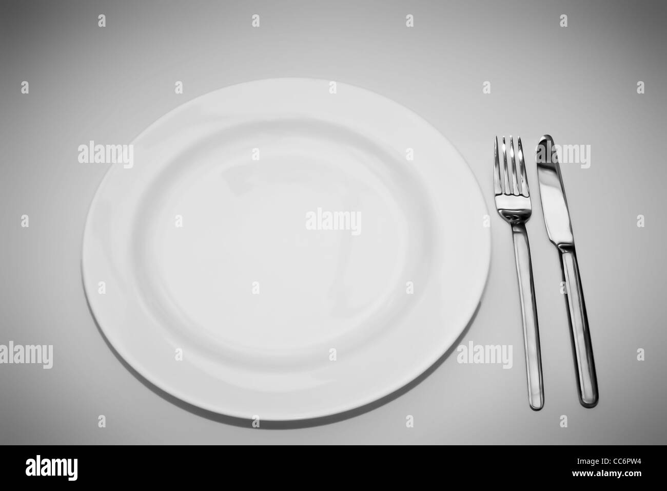 White plate with fork and knife over shaded white background Stock Photo