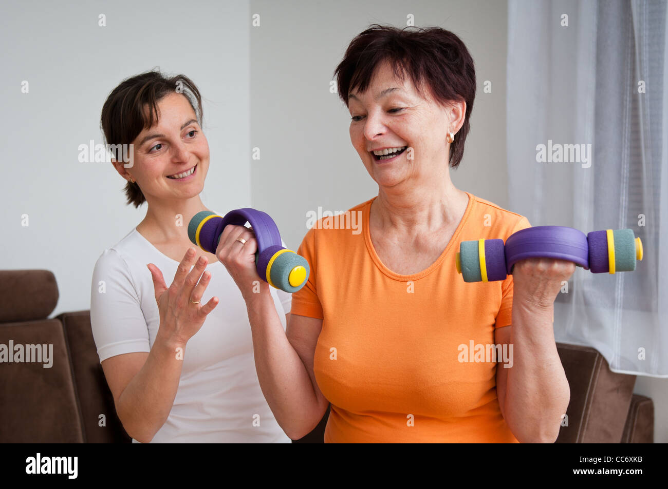 Coach assisting senior woman exercising with barbells Stock Photo